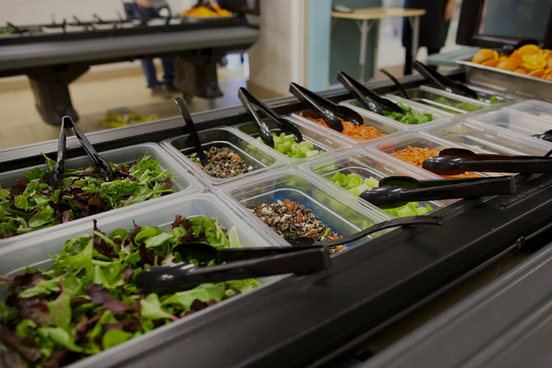 Campers' salad bar in a camp dining hall, trays of fresh greens, chopped vegetables and toppings set out for service